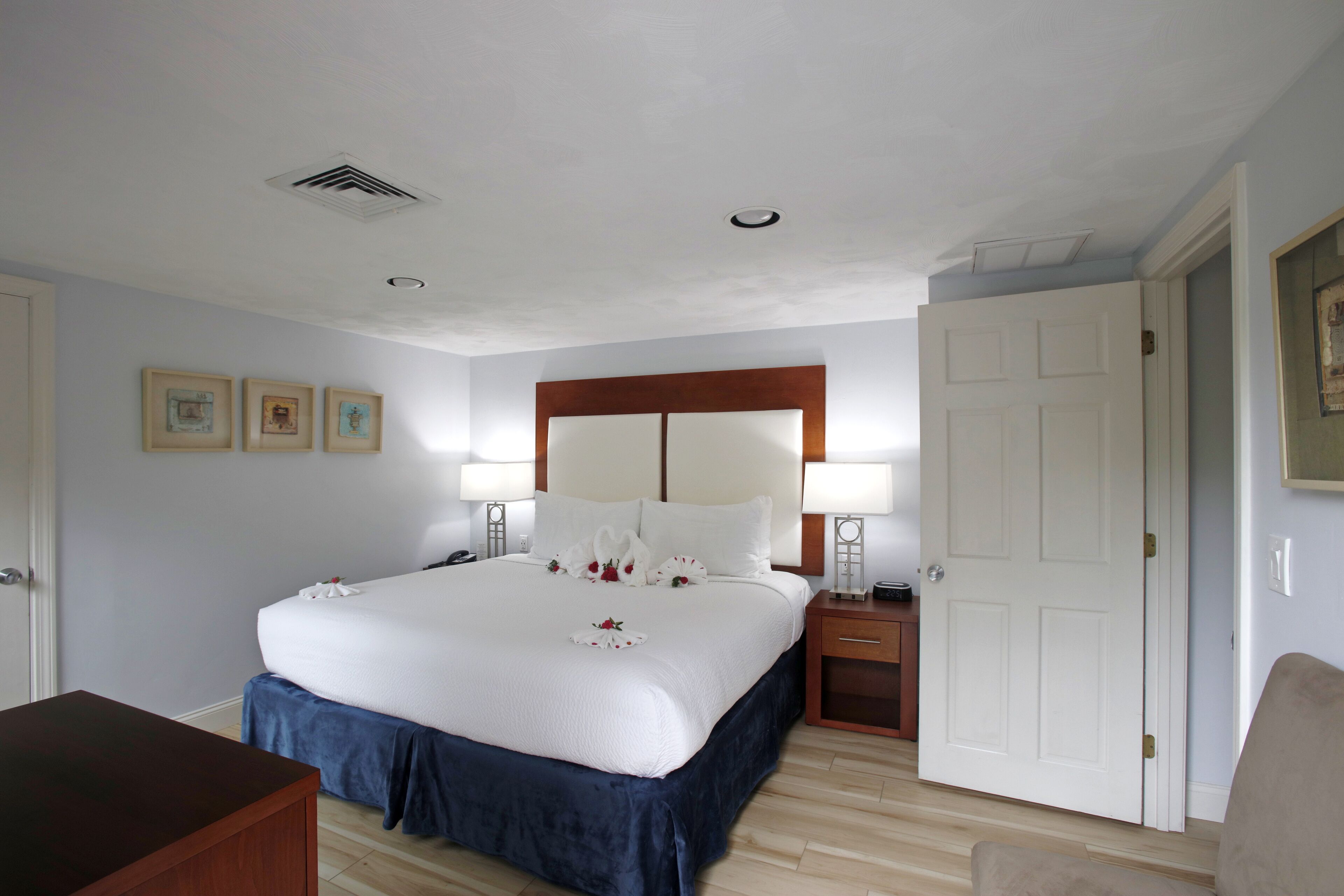 A hotel room with a large bed, bedside tables with lamps, a wooden headboard, and a door.