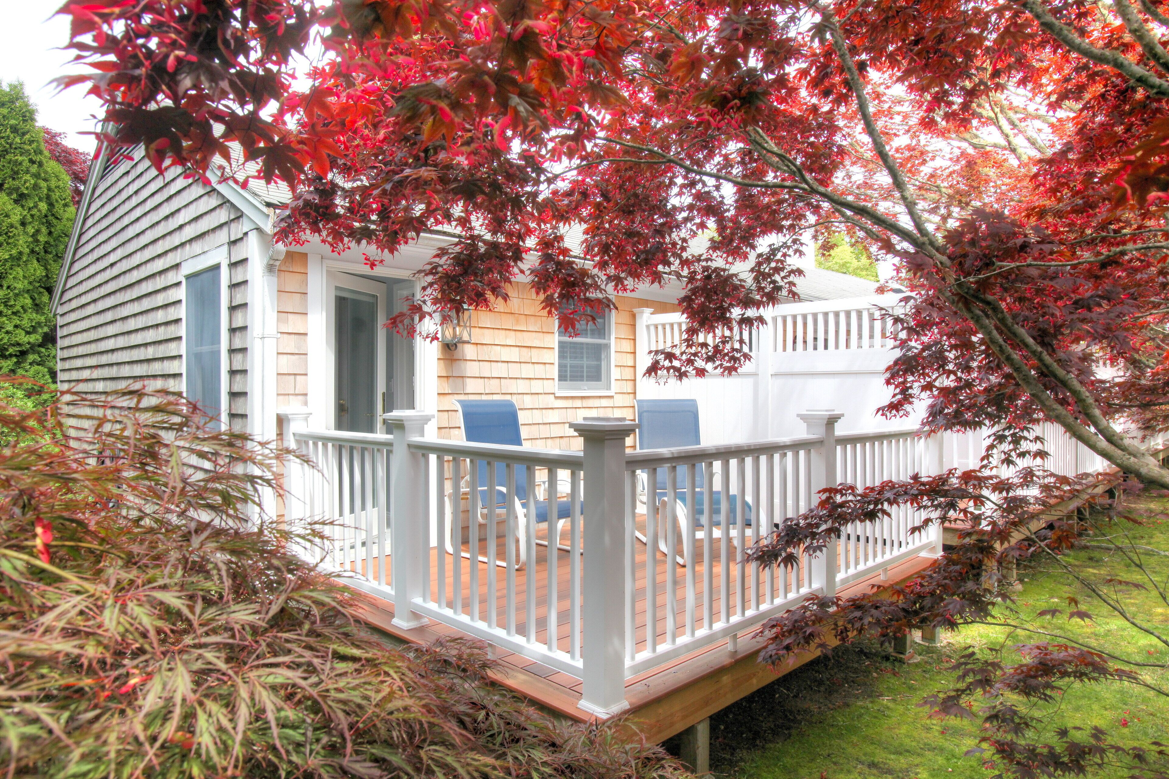A house with a wooden deck, two blue chairs, and a white railing.