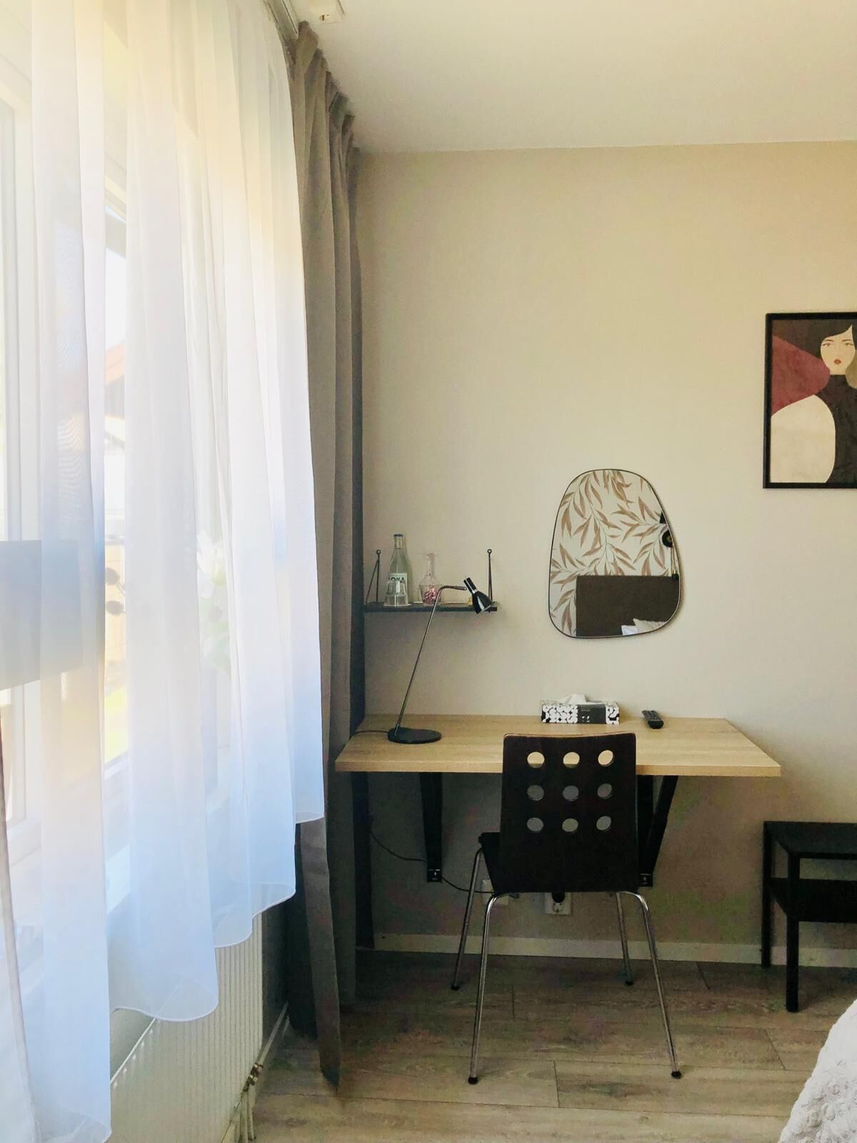 A room with a wooden desk, a chair, a mirror, and a shelf with items.