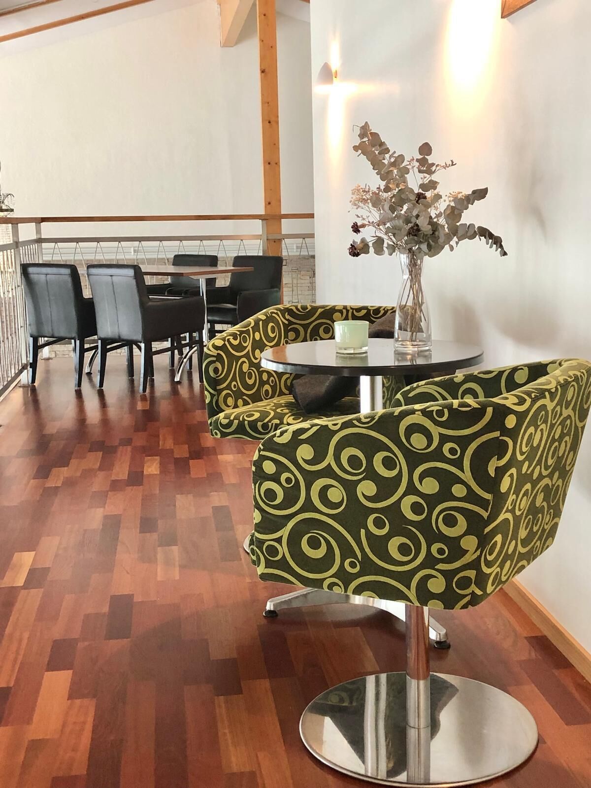 A dining area with a wooden floor, black chairs, a round table with a vase of flowers, and a patterned ottoman.