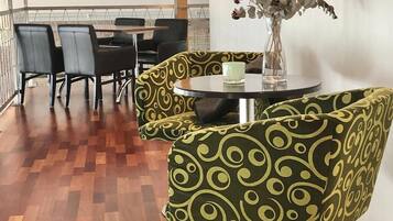 A dining area with a wooden floor, black chairs, a round table with a vase of flowers, and a patterned ottoman.