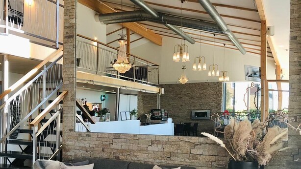 Amplia sala de estar con un sofá gris, una mesa de centro y un jarrón decorativo. Una escalera conduce a un nivel superior, y se observa una cocina al fondo.
