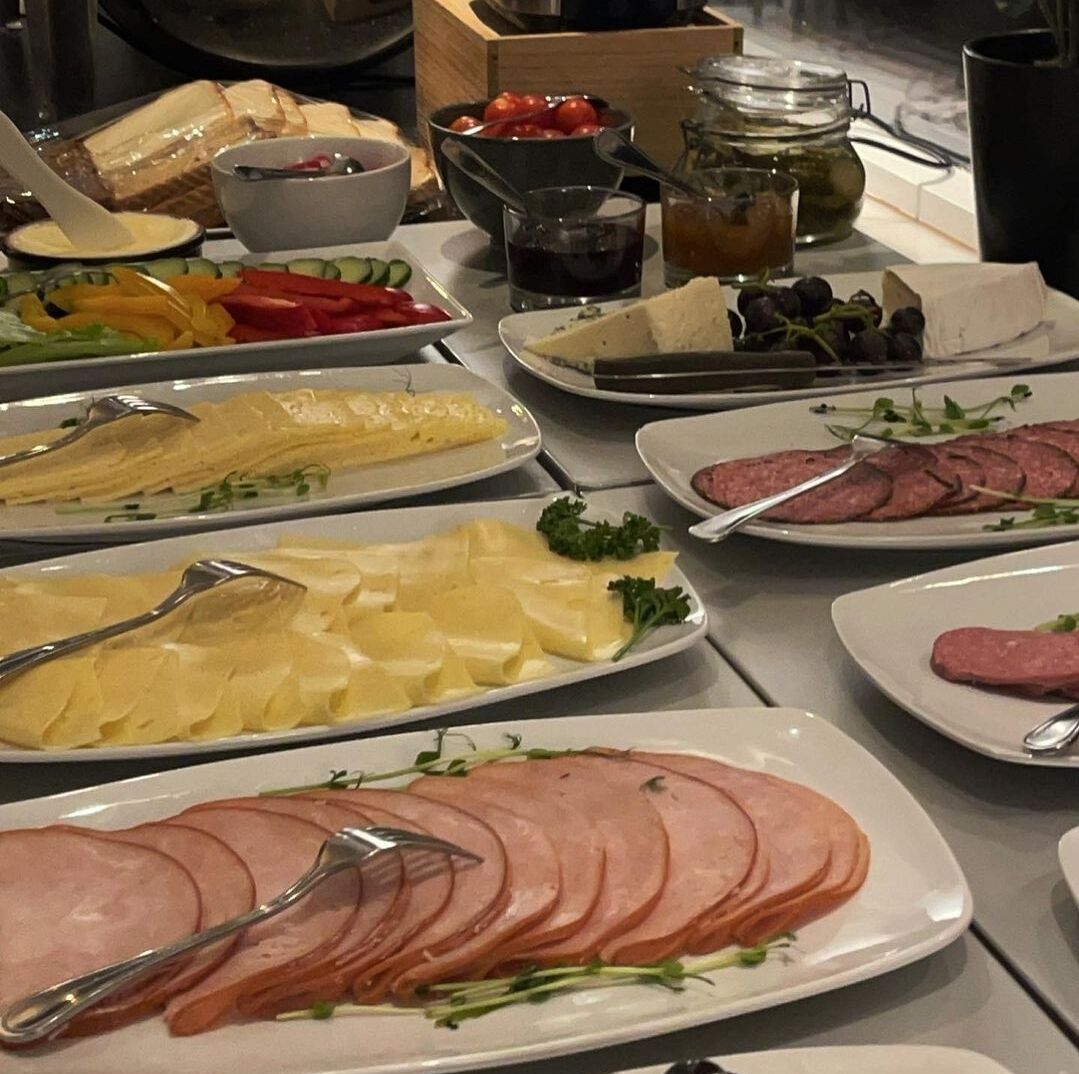 A buffet table with various dishes including sliced ham, cheese, and vegetables.