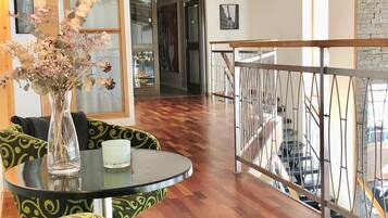 A modern interior with a wooden floor, a glass table, green patterned chairs, and a metal railing overlooking a staircase.