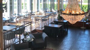Un restaurante espacioso con techos altos, amplias ventanas y un llamativo candelabro de cristal. Mesas y sillas dispuestas para comer.
