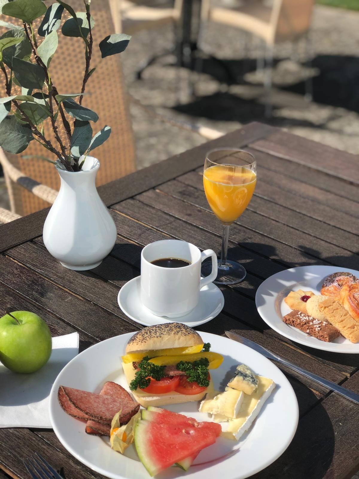 Una mesa con un almuerzo que incluye un sándwich, un vaso de jugo de naranja, una taza de café y un plato con varios pasteles.