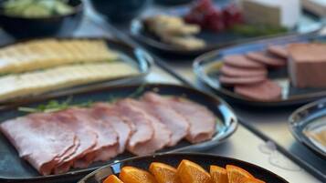 Una mesa con diversos alimentos, como jamón en rodajas, naranjas y uvas.