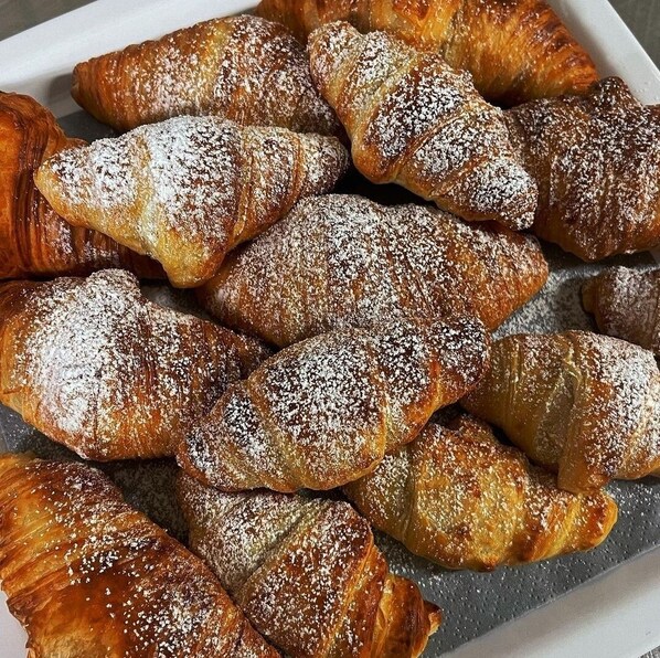 Una bandeja con varios pasteles, incluyendo croissants y otras exquisiteces horneadas, espolvoreados con azúcar glas.
