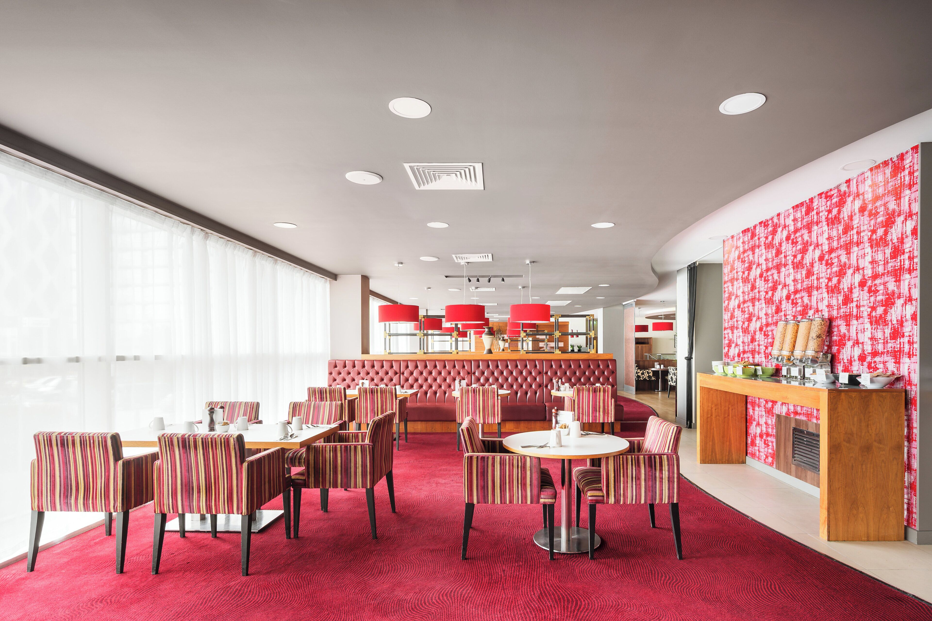 Un restaurante moderno con sillas a rayas, alfombra roja y pared con estampado rojo y blanco.