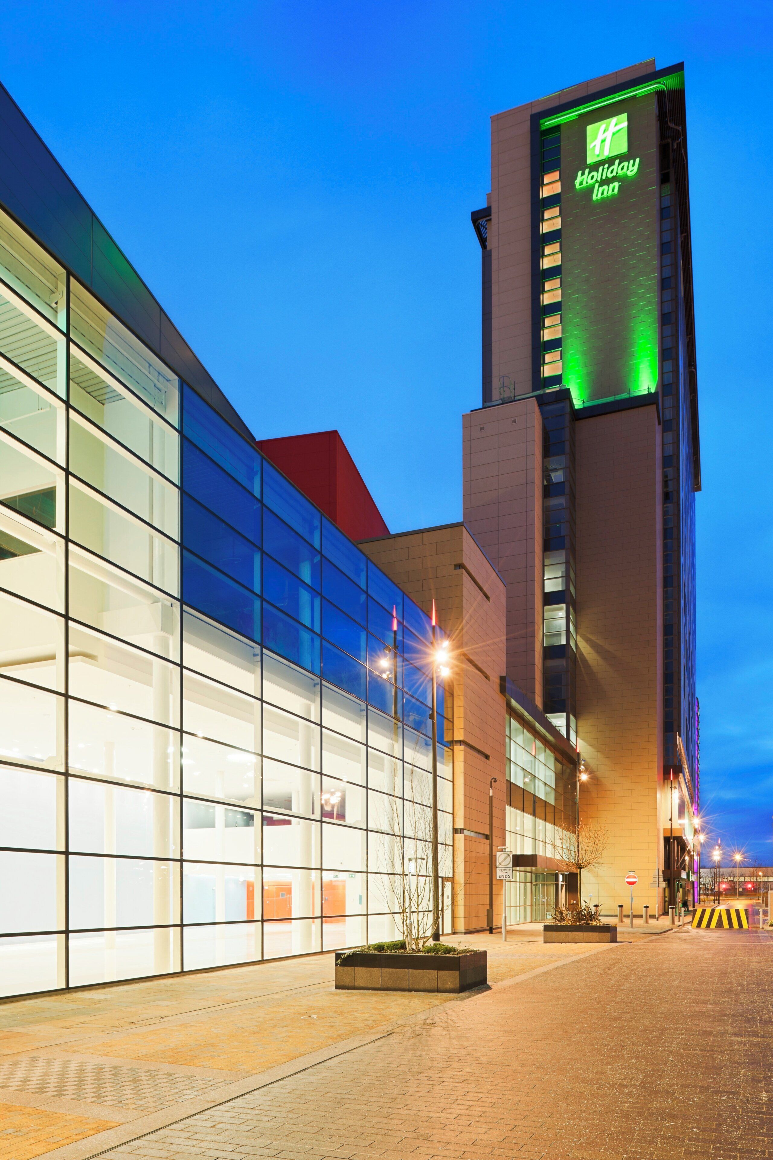 A Holiday Inn hotel with a modern glass facade and a prominent green-lit sign on the tower.