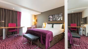 Une chambre d’hôtel équipée d’un lit, d’un bureau, d’une chaise, d’un banc, d’une lampe et d’un téléviseur fixé au mur.