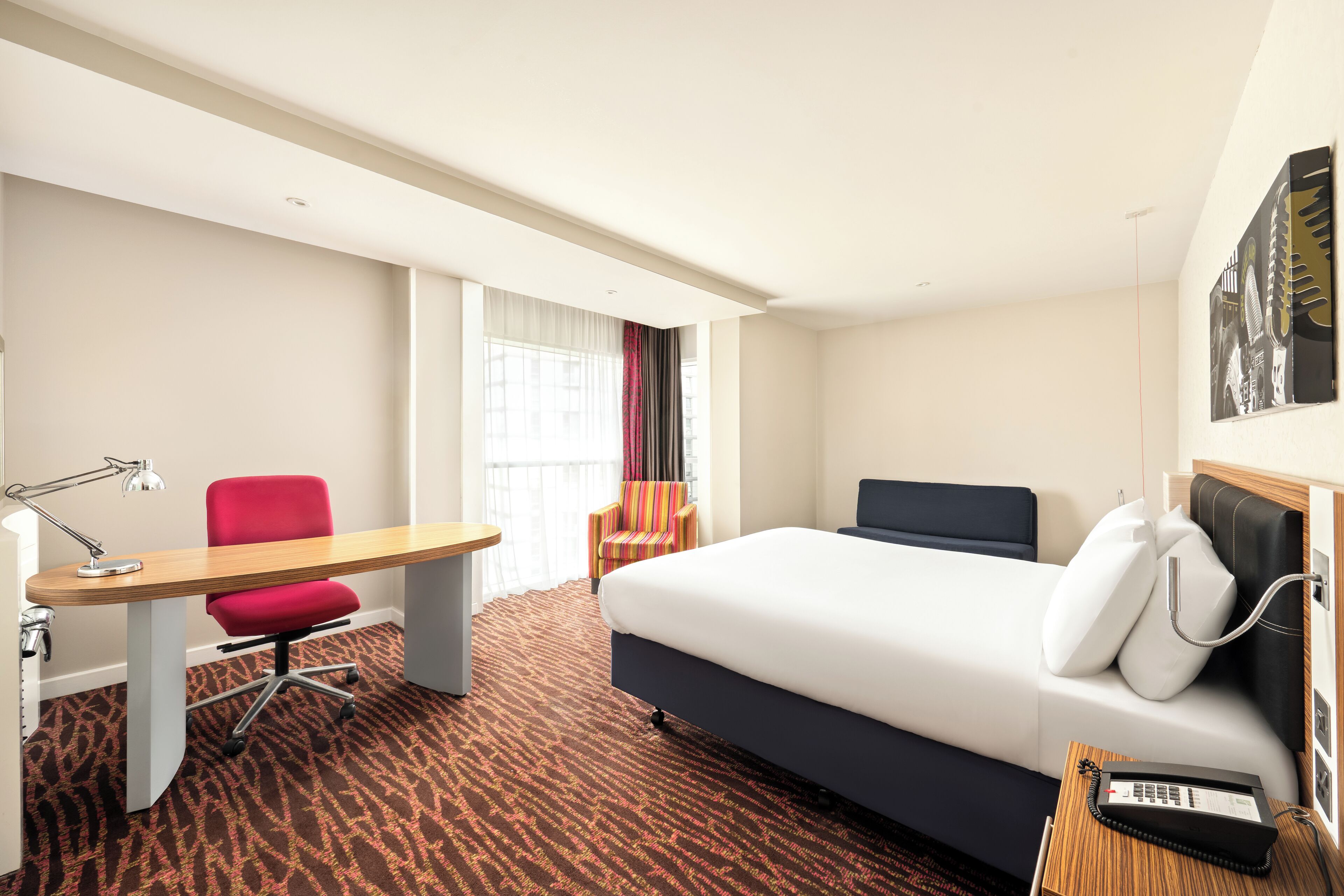 Habitación de hotel con cama, escritorio, silla y teléfono.