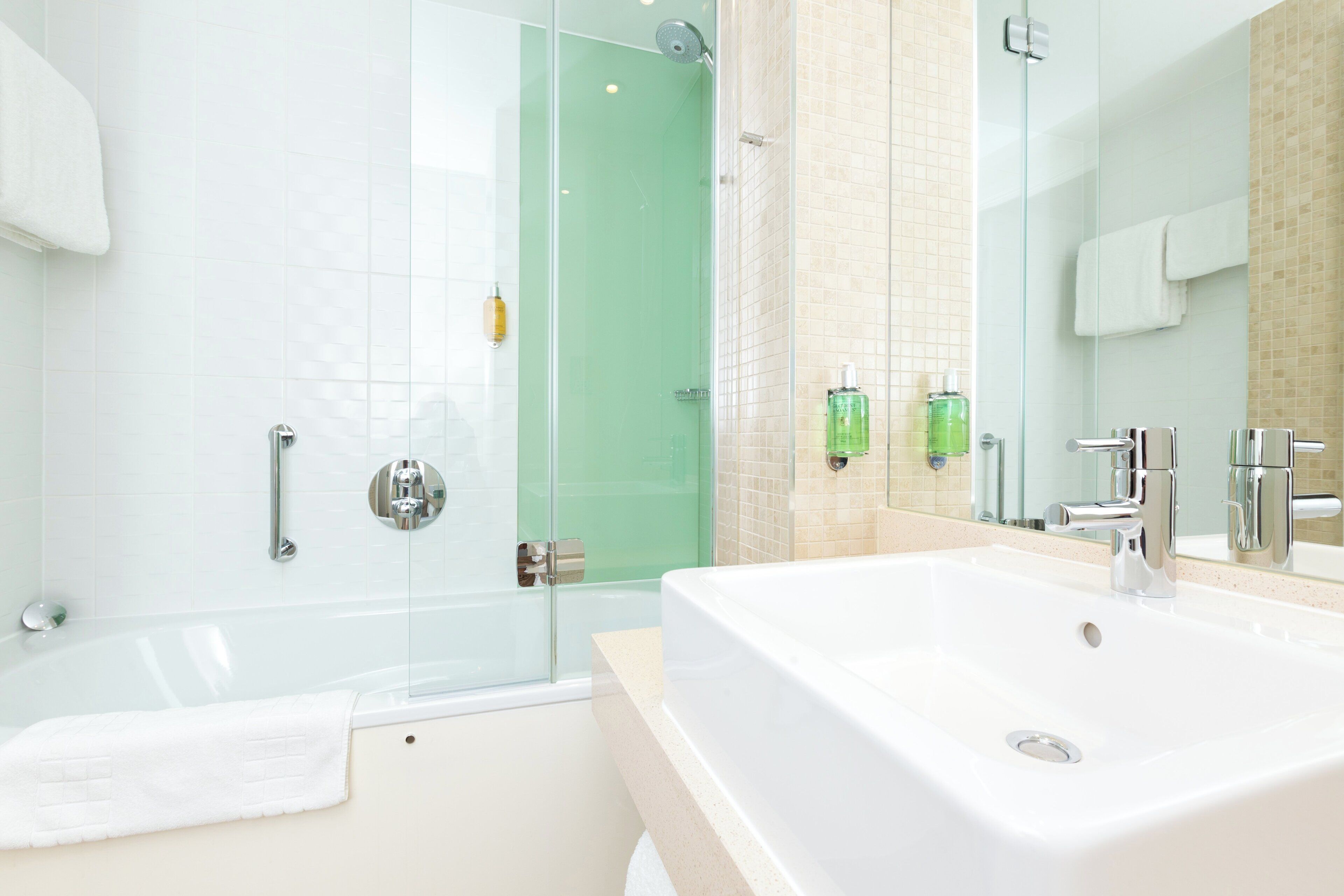 A modern bathroom with a glass-enclosed shower, a large white bathtub, and a sink with a mirror.