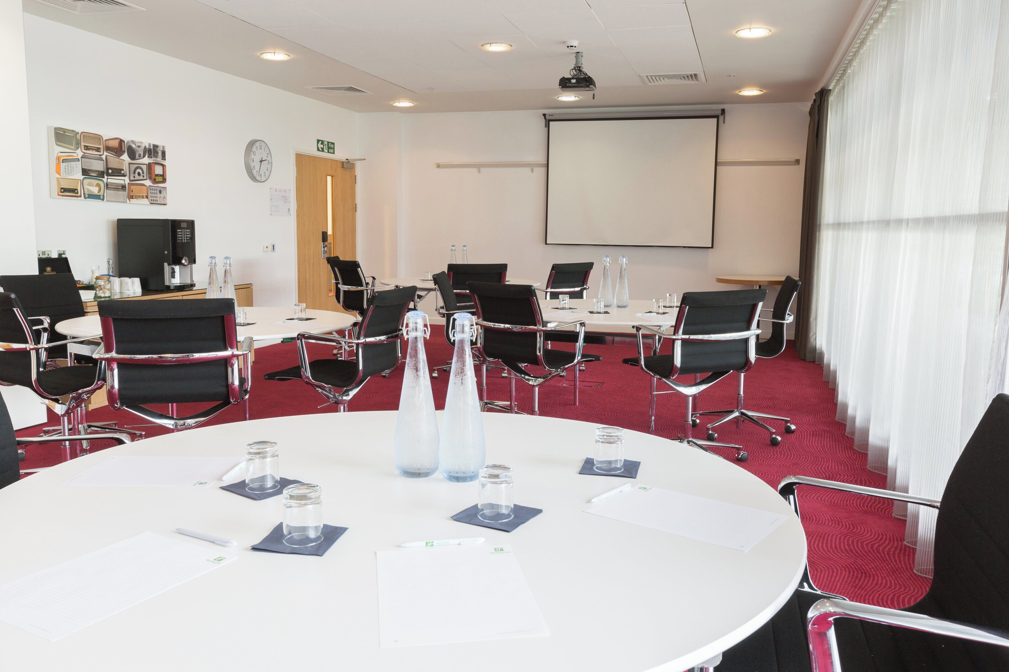 A conference room with a white table, black chairs, a projector screen, and a red carpet.