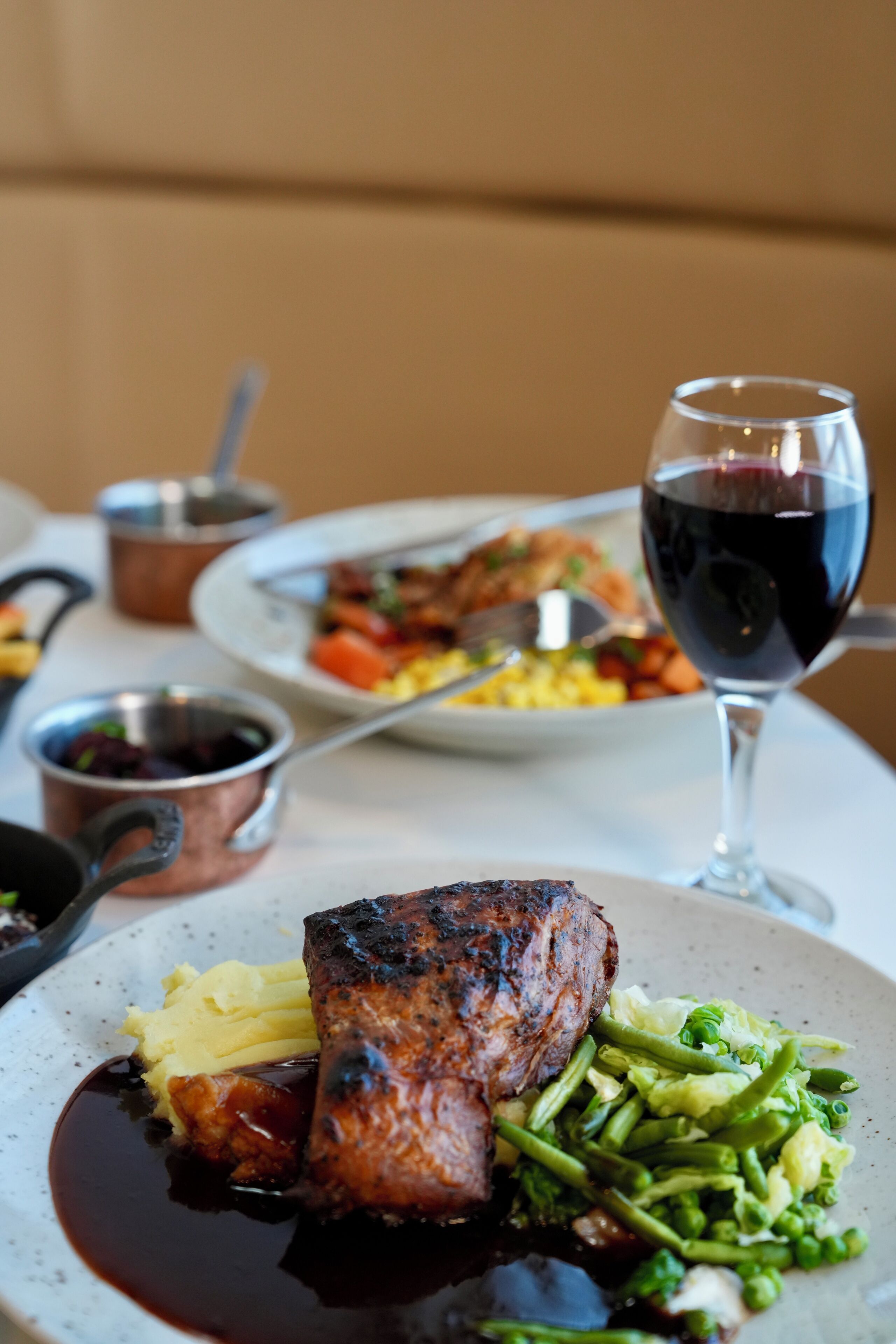 A dining table with a plate of food, a glass of red wine, and a copper pot.