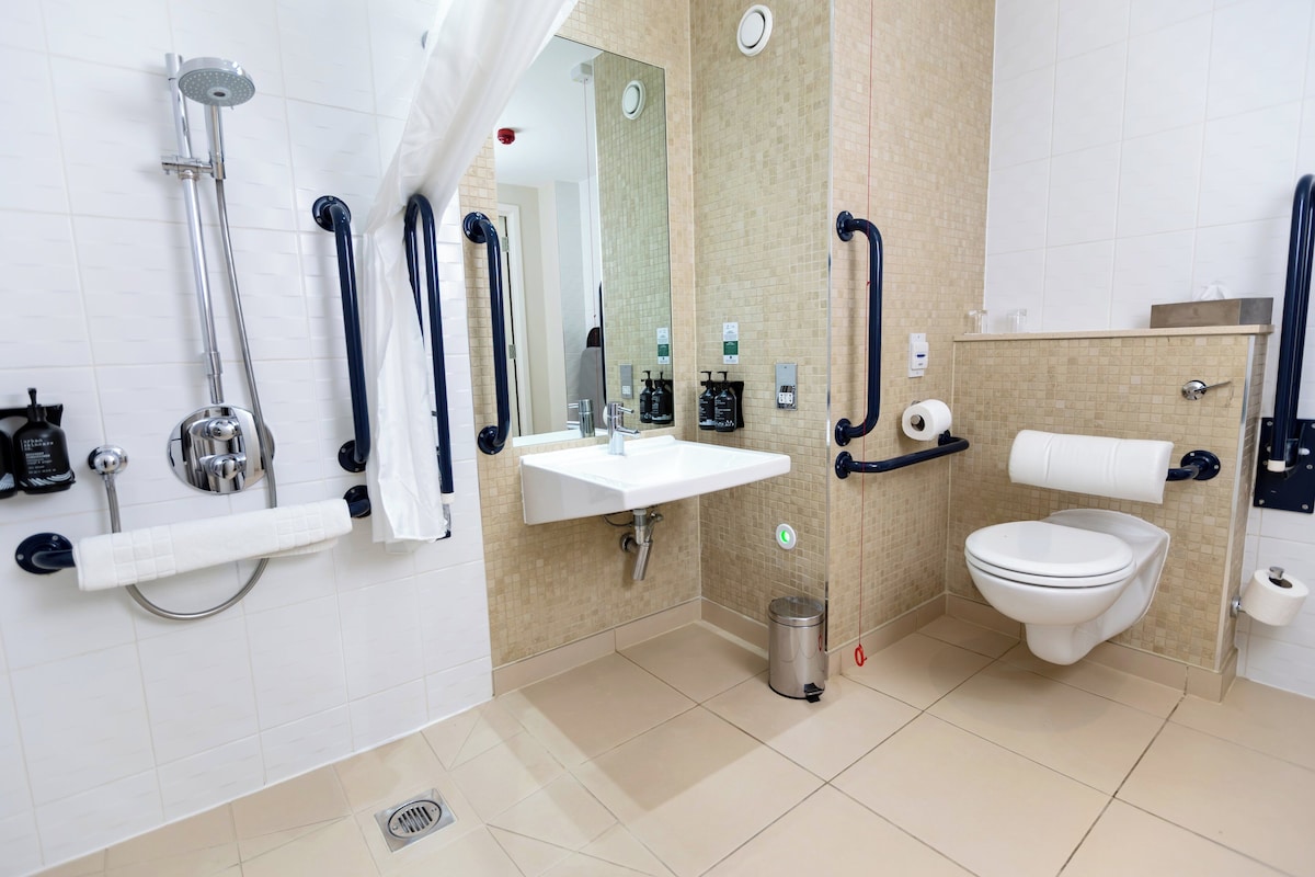 Un baño moderno con ducha, lavamanos, inodoro y barras de apoyo.