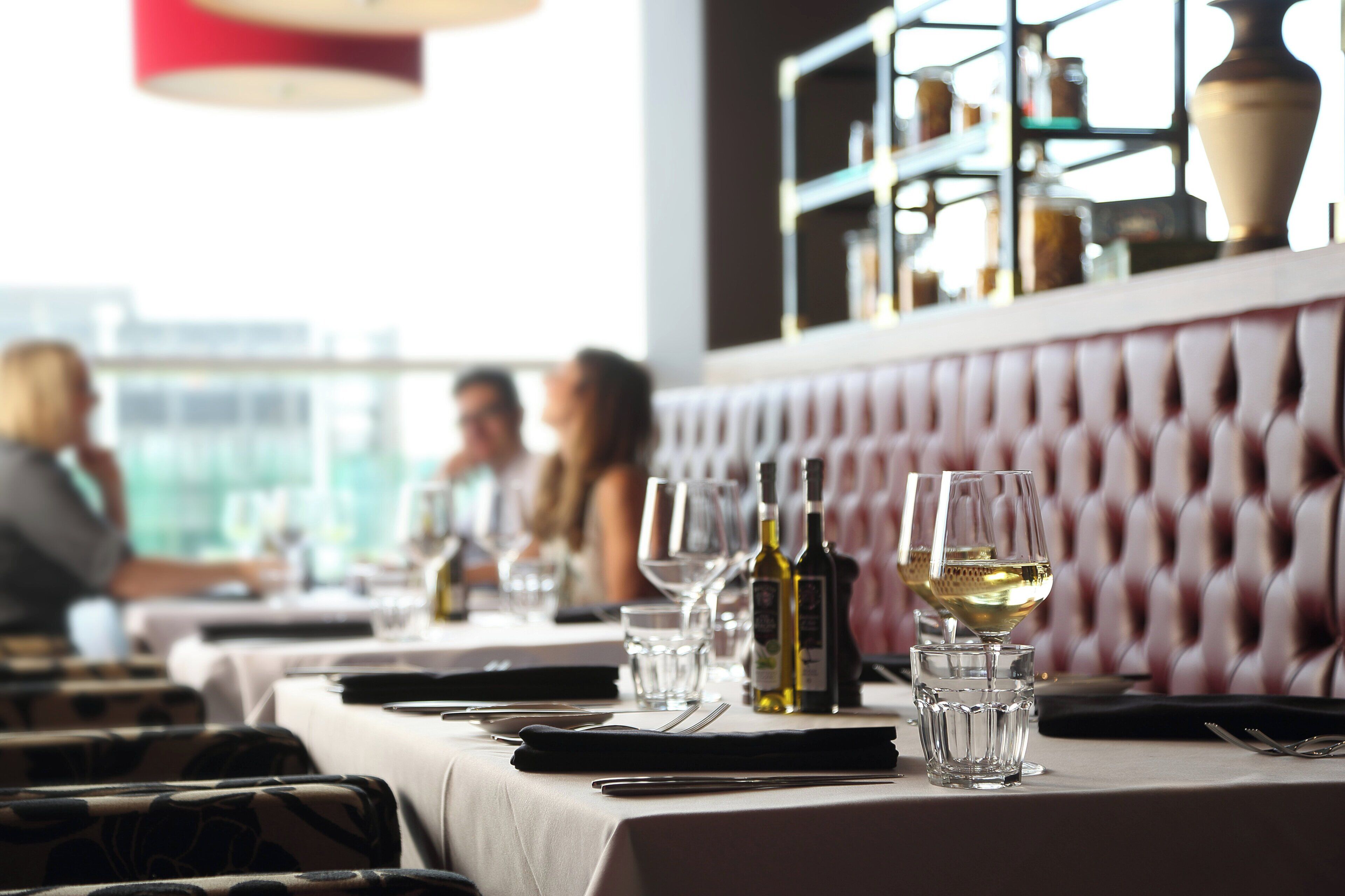 Un interior de restaurante con una mesa lista para comer, copas y botellas de vino.