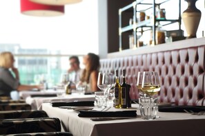 A restaurant interior with a table set for dining, glasses, and bottles of wine. - Holiday Inn Manchester-Media City UK by IHG (Salford)