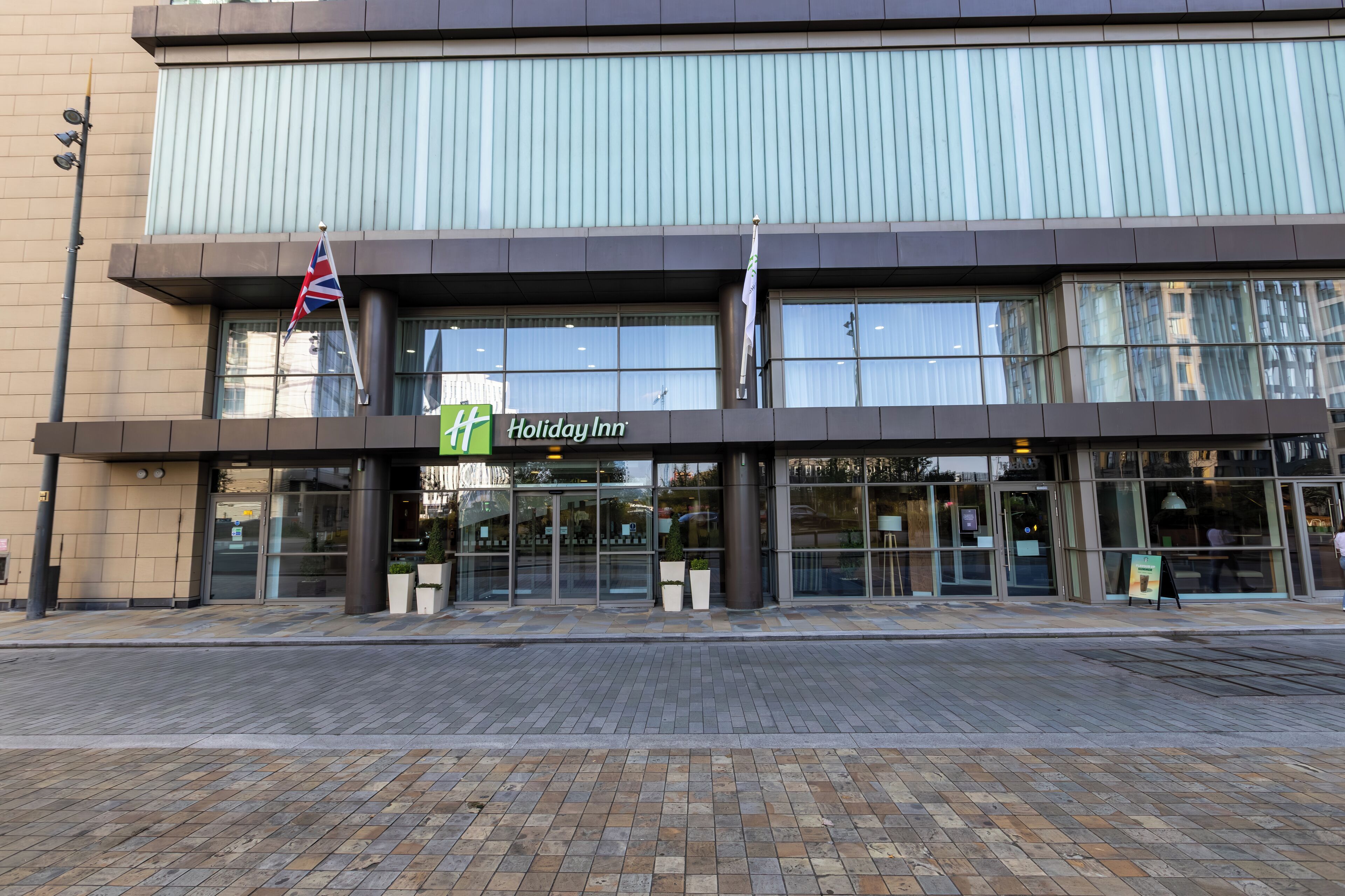 A Holiday Inn hotel with a modern facade, large glass windows, and a flagpole with flags.