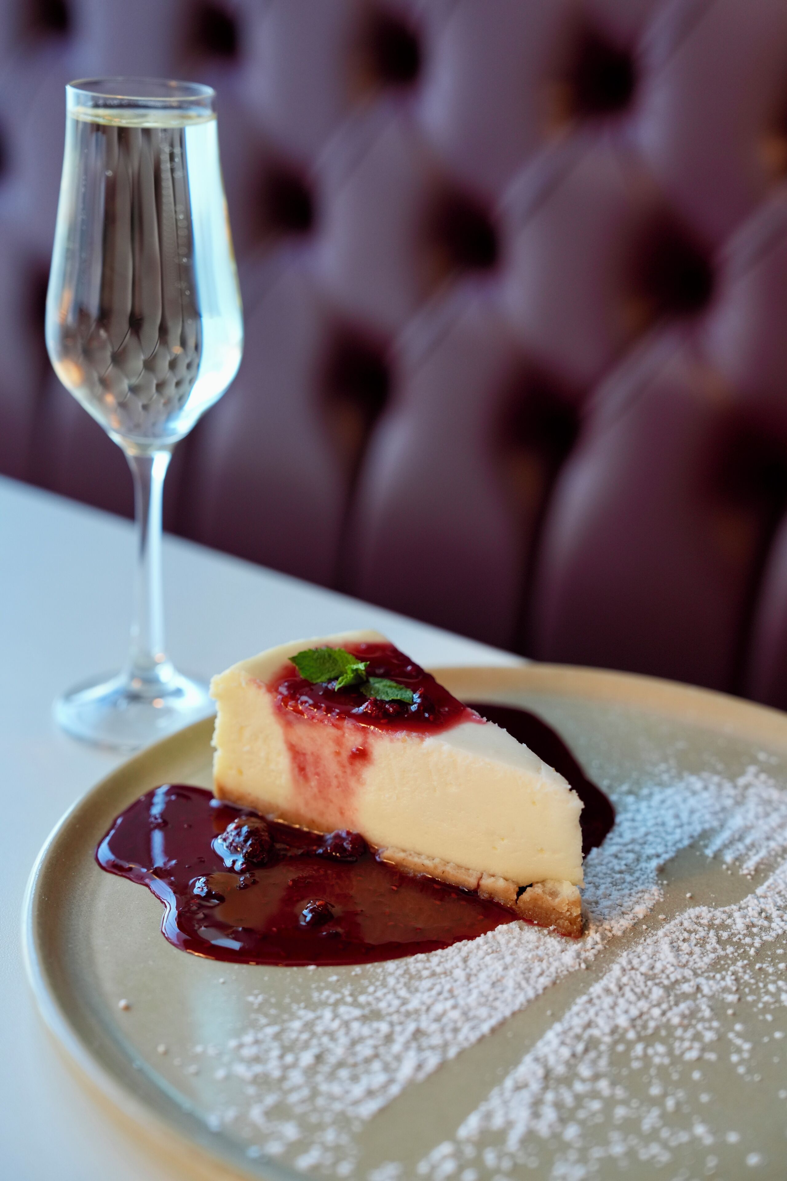 A dessert with a berry compote and powdered sugar on a plate, accompanied by a glass of water.