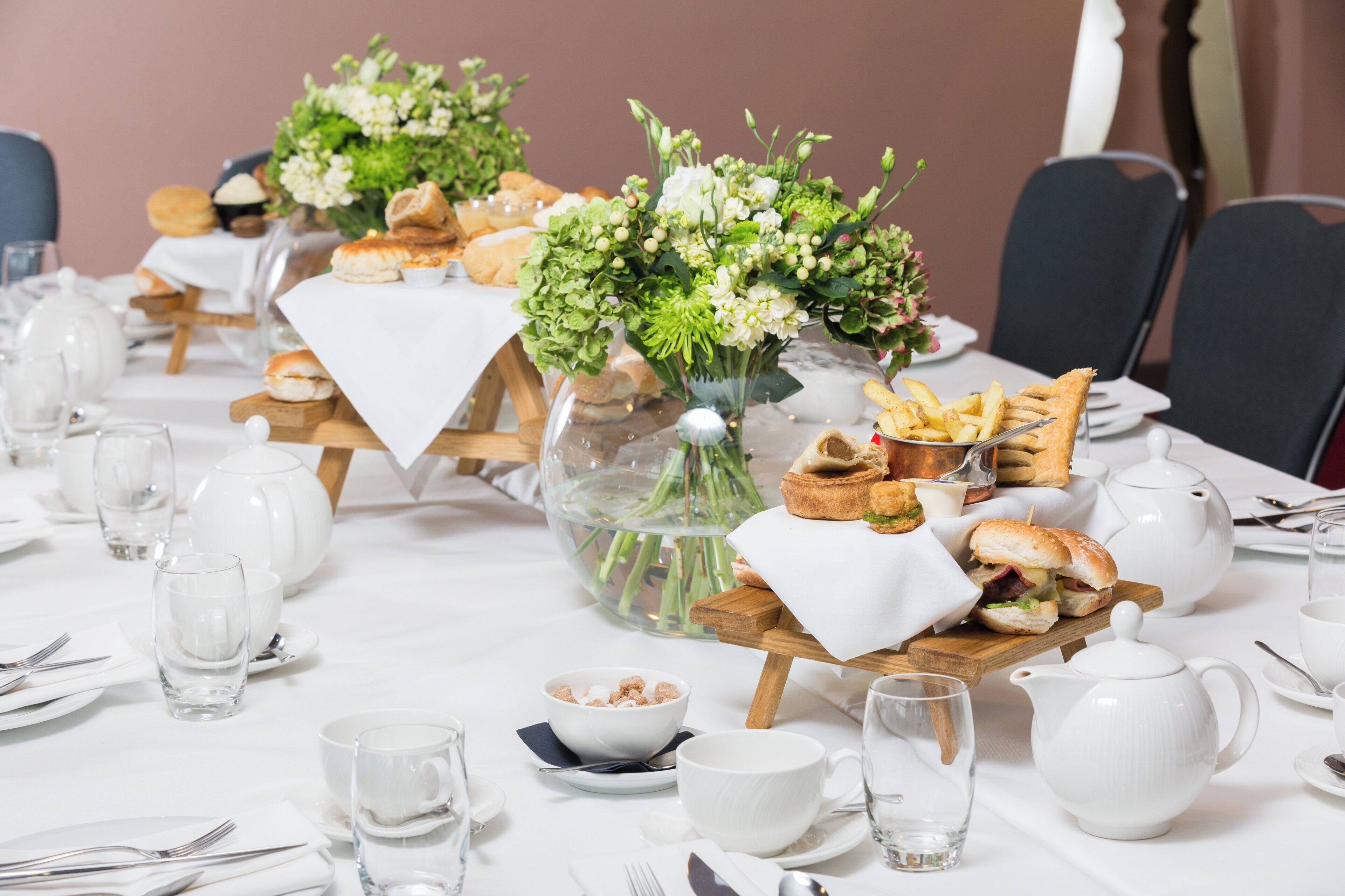 A dining table set with white tablecloths, glassware, and a centerpiece with flowers and bread.
