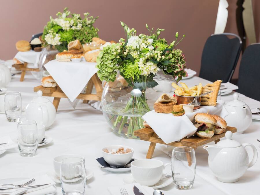 A dining table set with white tablecloths, glassware, and a centerpiece with flowers and bread.