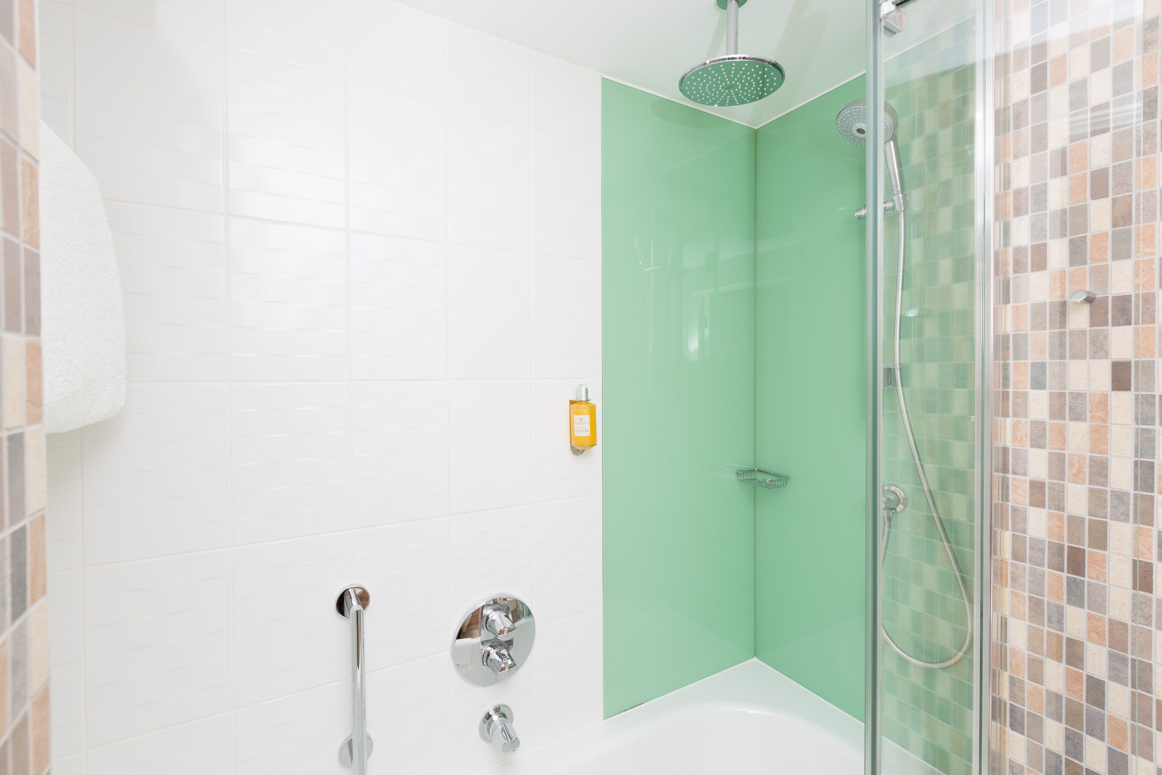 Een moderne badkamer met een douchecabine van glas, een wit bad en een groene accentmuur.
