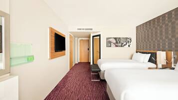Ett hotellrum med två sängar, en tv, ett konstverk som hänger på väggen och ett golv täckt av matta.