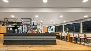 Zona de bar moderna amb un taulell negre, llums penjants i un espai de seients amb cadires de fusta.