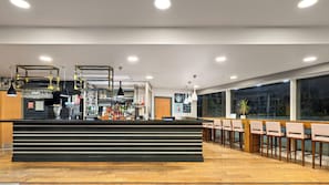 A modern bar area with a black counter, hanging lights, and a seating area with wooden chairs.