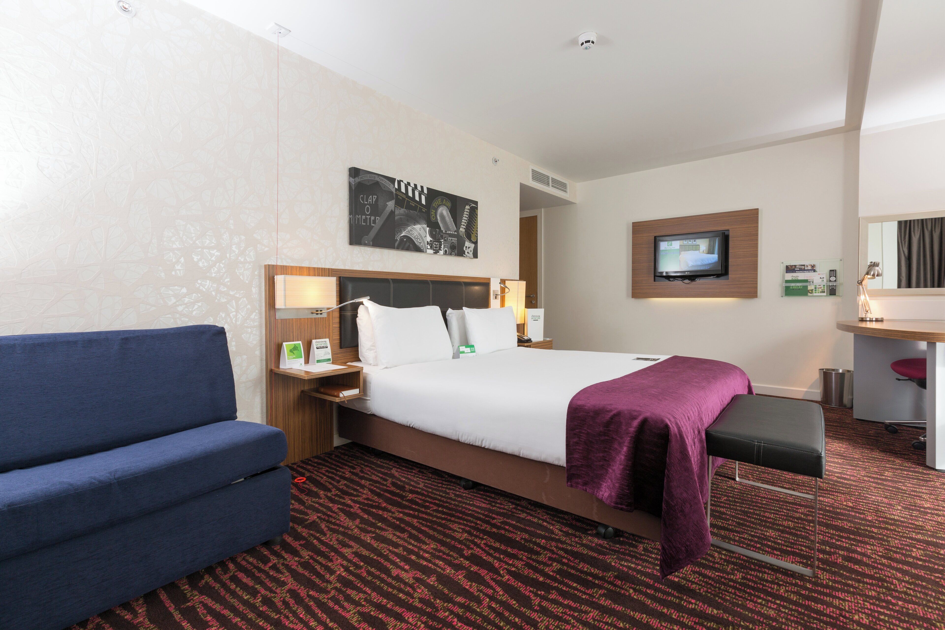 Habitación de hotel con cama, escritorio, silla, televisión y una obra de arte colgada en la pared.
