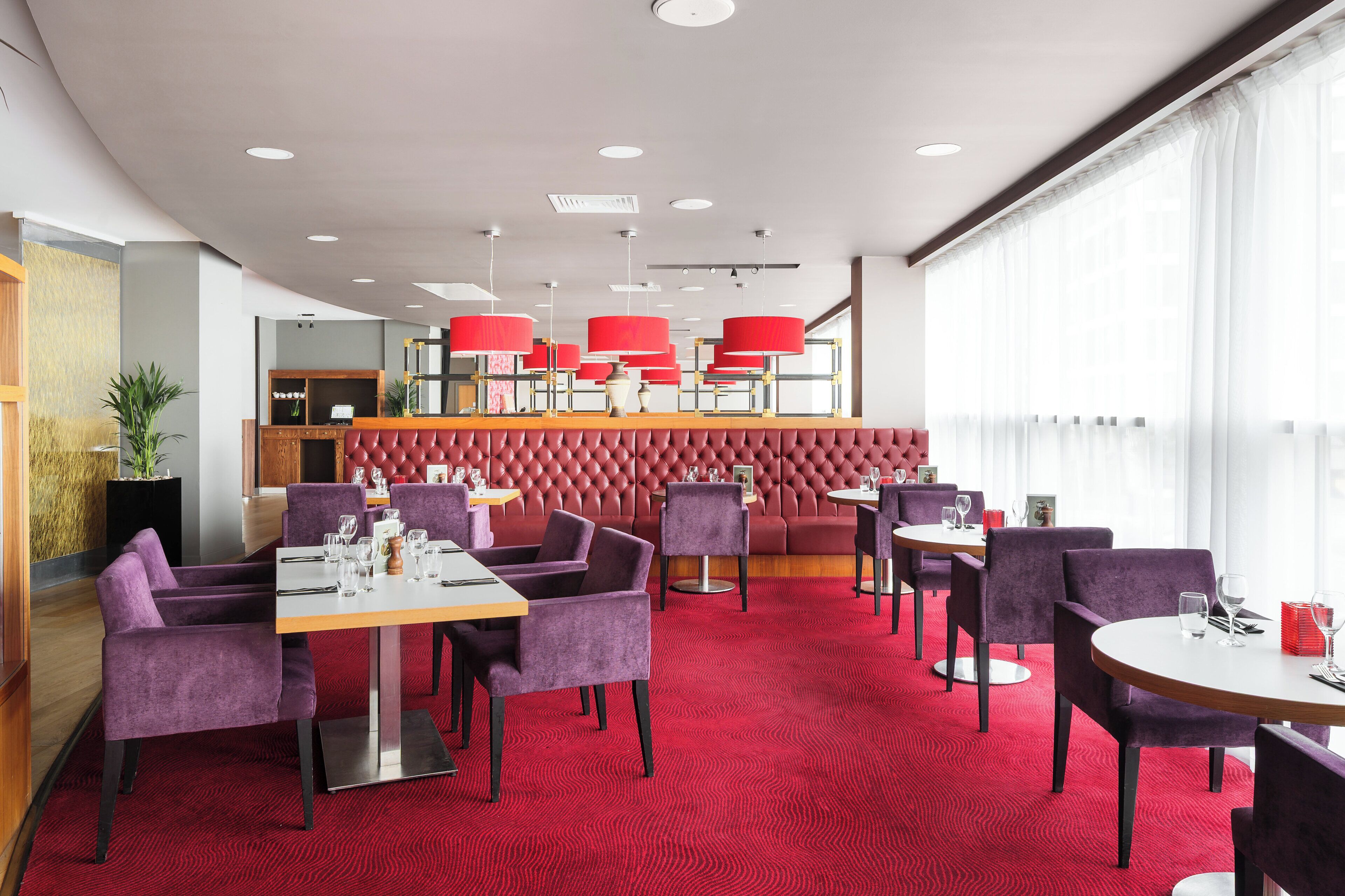 Um restaurante moderno com piso de carpete vermelho, assentos roxos e luminárias pendentes vermelhas.