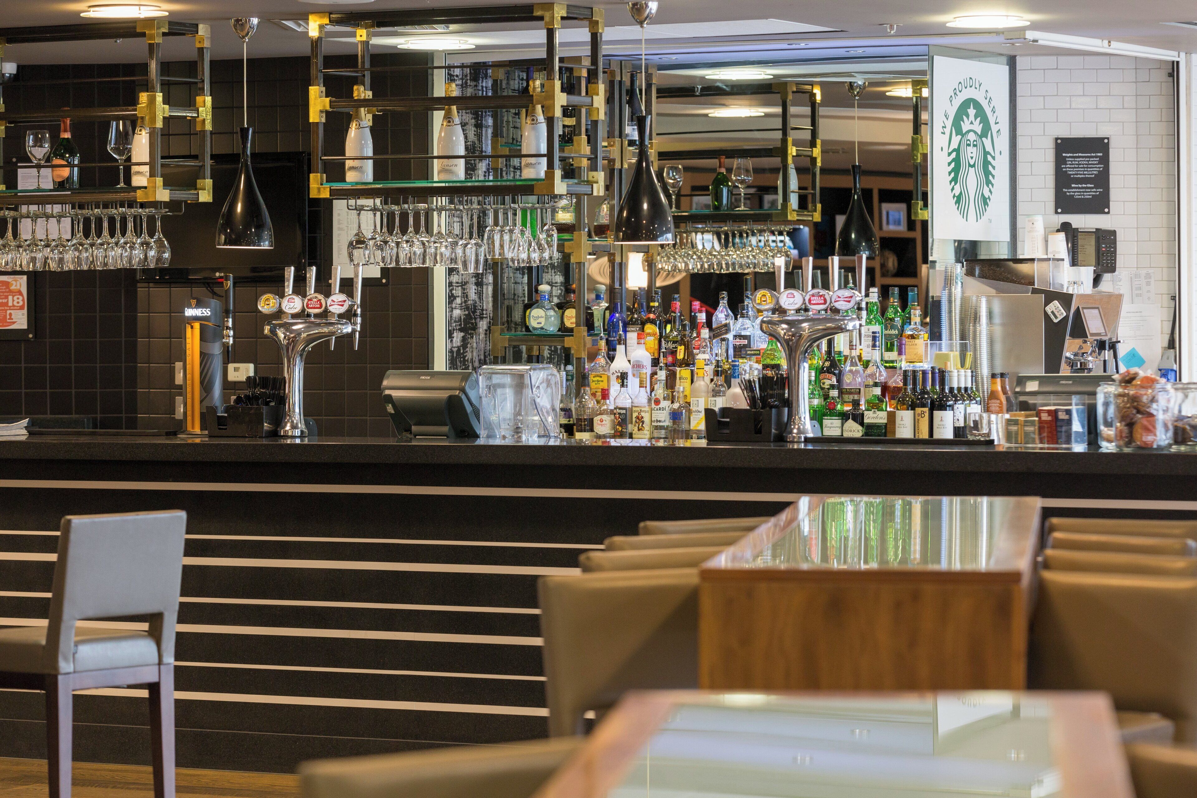 Zona de bar con varias botellas de licor, vasos y un letrero de Starbucks.