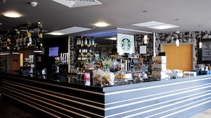 A bar area with a counter, shelves of bottles, and a menu board. - Holiday Inn Manchester-Media City UK by IHG (Salford)