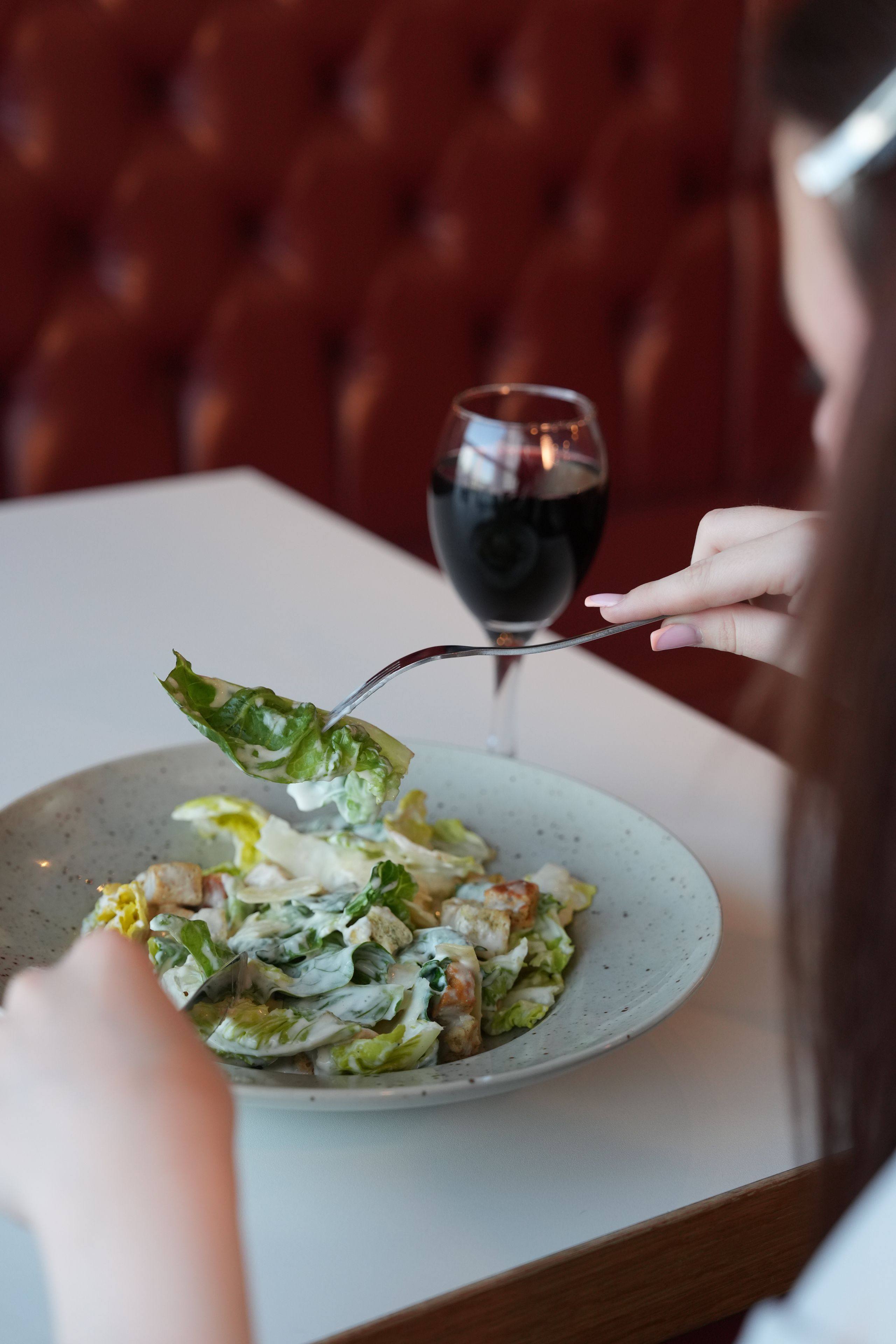 A person dining at a table with a plate of food and a glass of red wine.
