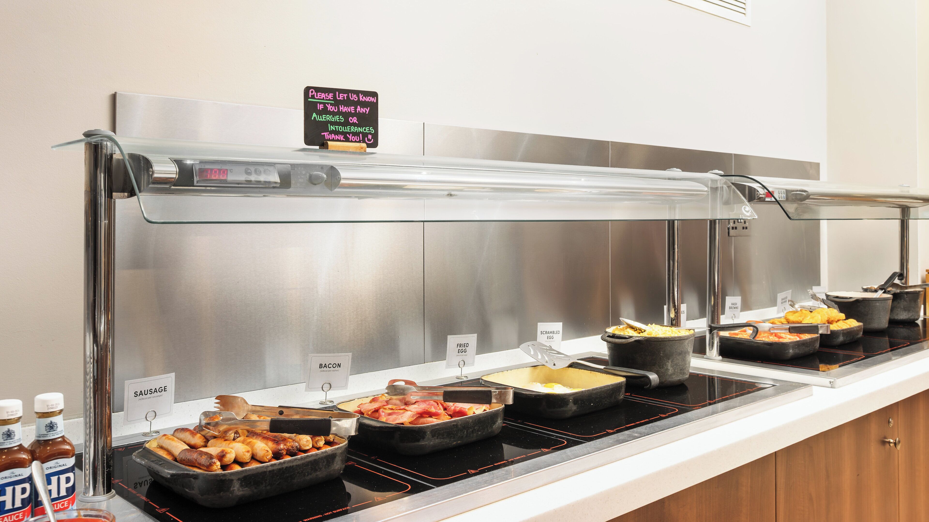 A buffet with various food options including bacon, sausage, fried eggs, scrambled eggs, and baked beans.