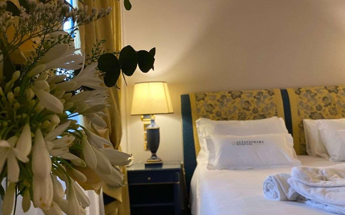 Una habitación de hotel con una cama bien hecha, una lámpara de noche y un arreglo floral.