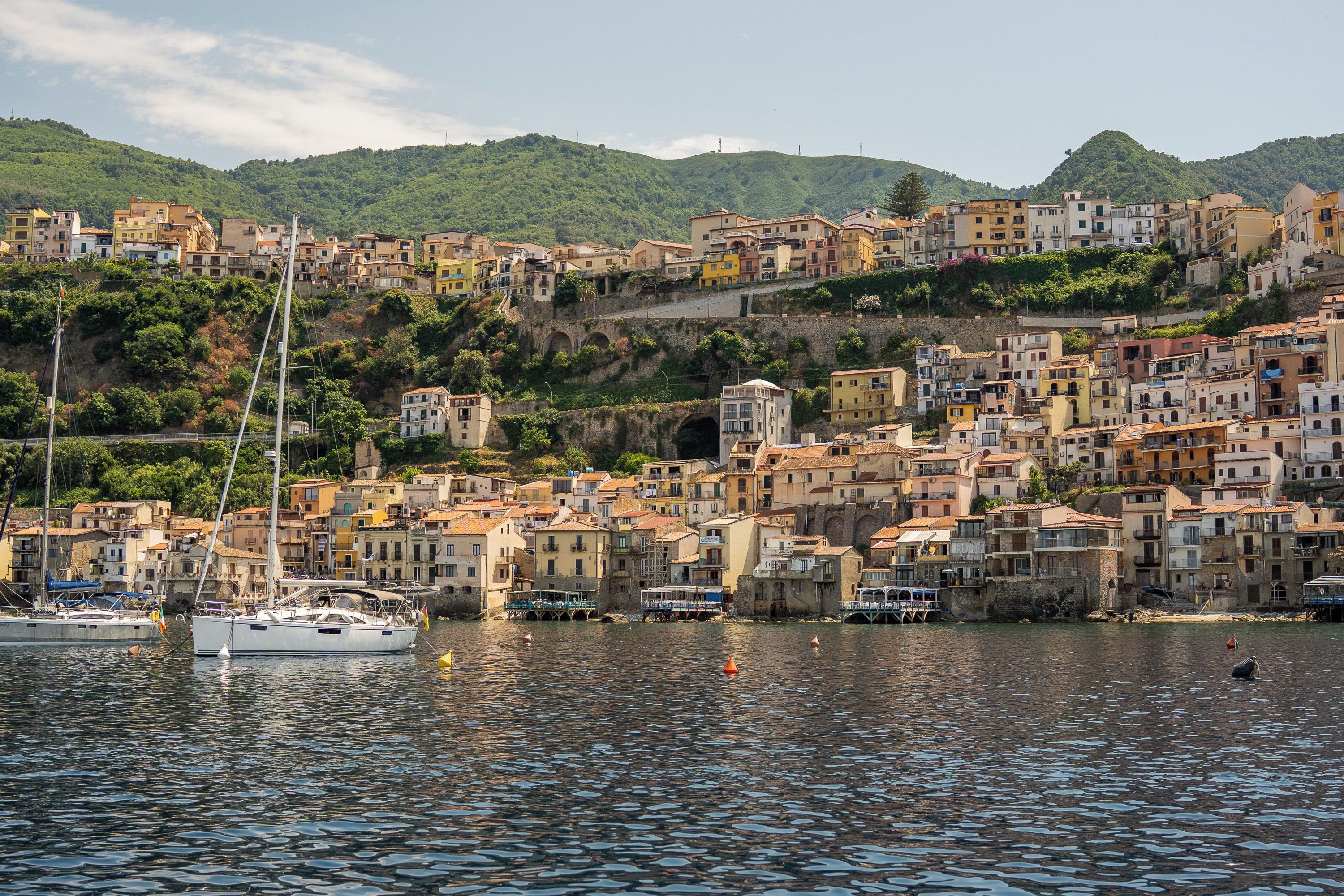 A coastal town with buildings along the waterfront, a clear sky, and a hilly backdrop.