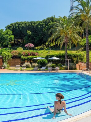 A swimming pool with clear blue water, surrounded by lounge chairs and umbrellas, with palm trees and greenery in the background. - Altafiumara Resort & Spa (Villa San Giovanni)