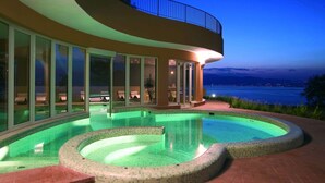 Une maison moderne dotée d’une grande piscine et offrant une vue sur la mer au crépuscule.