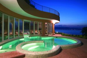Et moderne hus med en stor swimmingpool og havudsigt i skumringen.