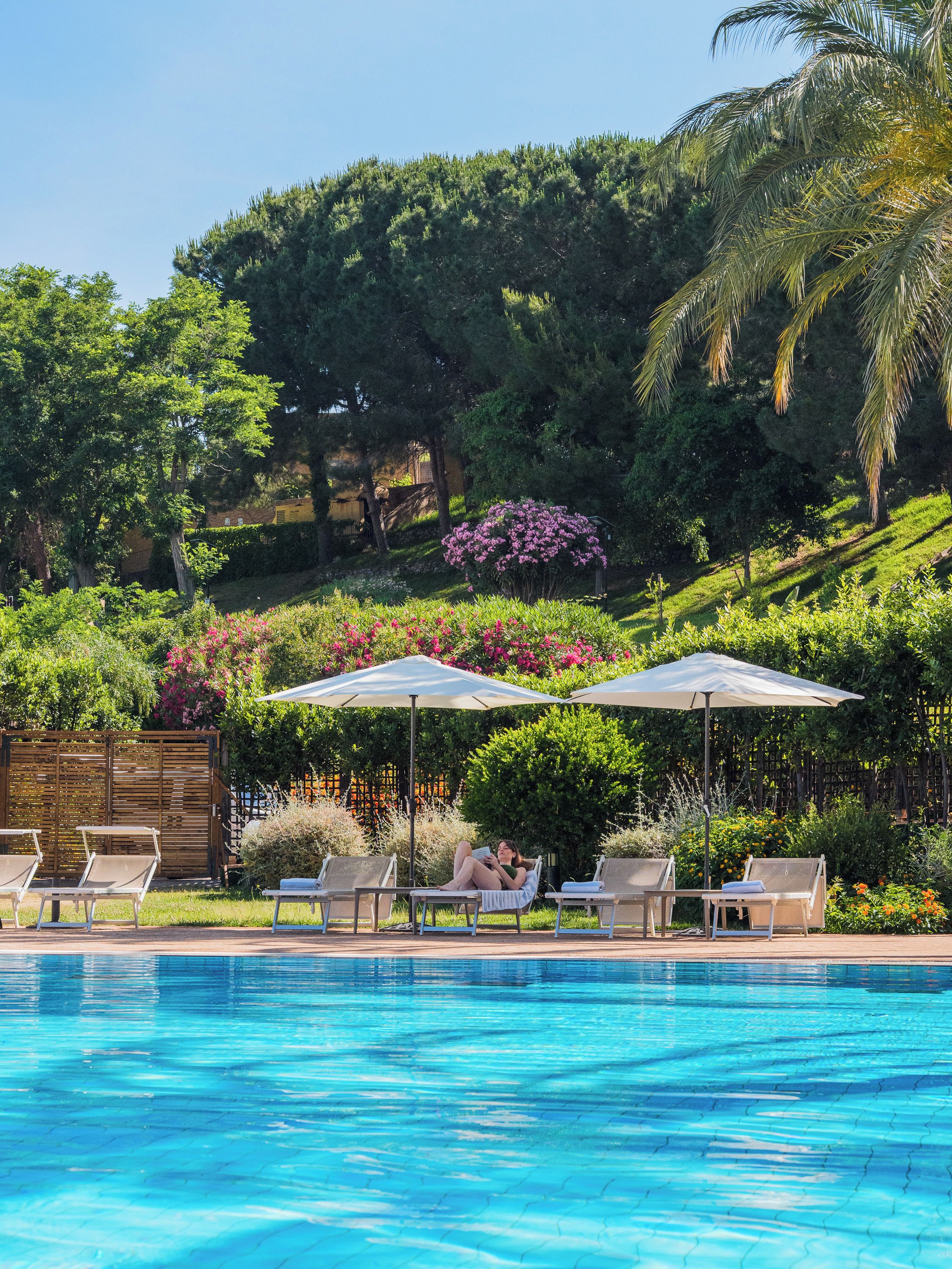 A swimming pool with lounge chairs and umbrellas, surrounded by lush greenery and trees.