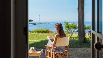 A person seated in a chair with a view of the sea and a tree.