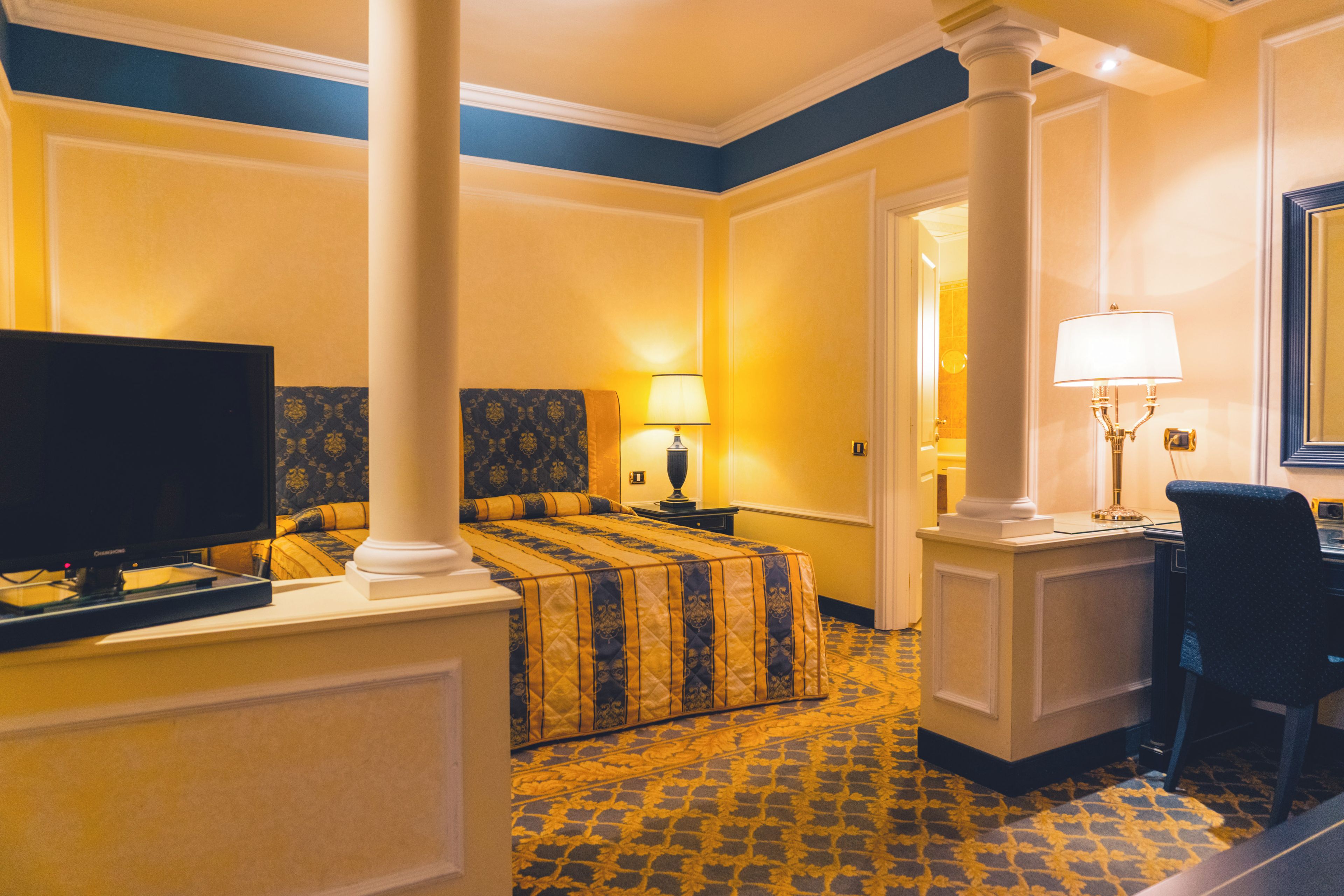 A hotel room with a bed, a desk, a chair, a television, and a lamp.