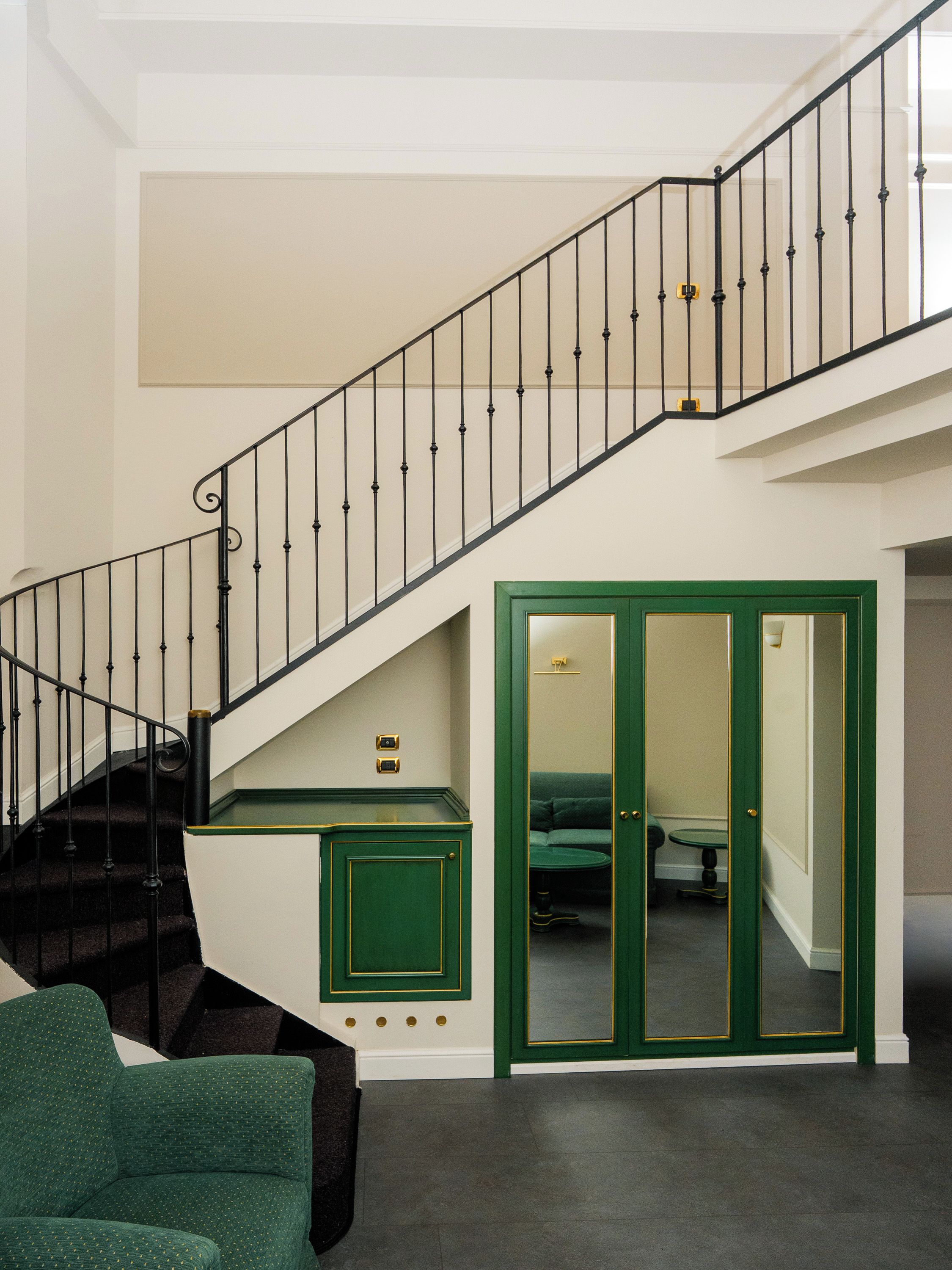 A staircase with black railings, a green door, and a green armchair.
