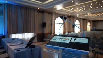 A presentation setup in a conference room with a laptop on a table, a tablet on a stand, and a speaker in the background.