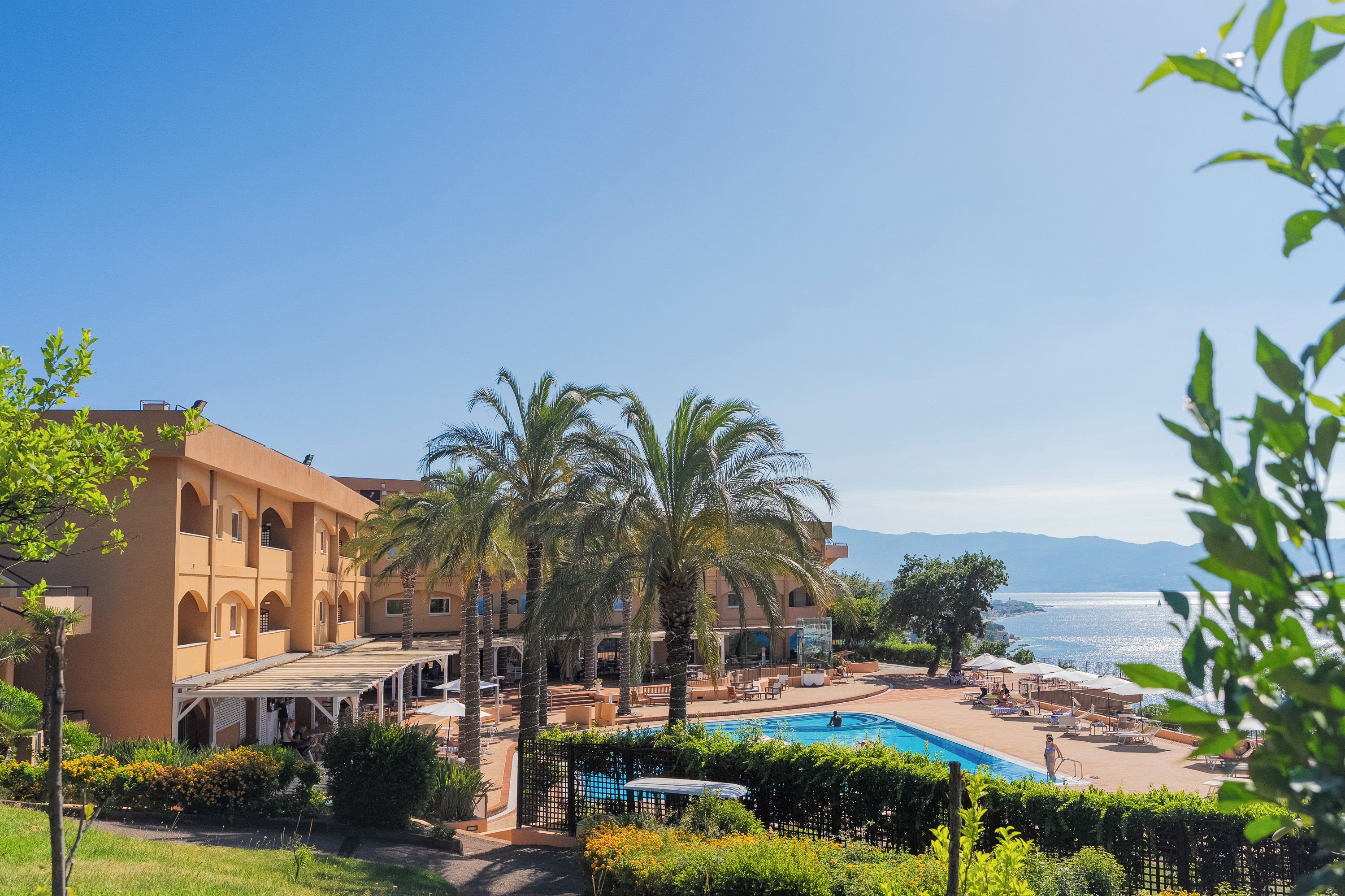 A resort with a pool, palm trees, and a view of the sea.