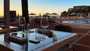 Un coin repas avec une table dressée pour deux personnes, donnant sur une piscine et des parasols de plage.