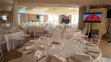 A banquet hall with round tables set for a formal event, clear chairs, and a large screen displaying an image of an apple.