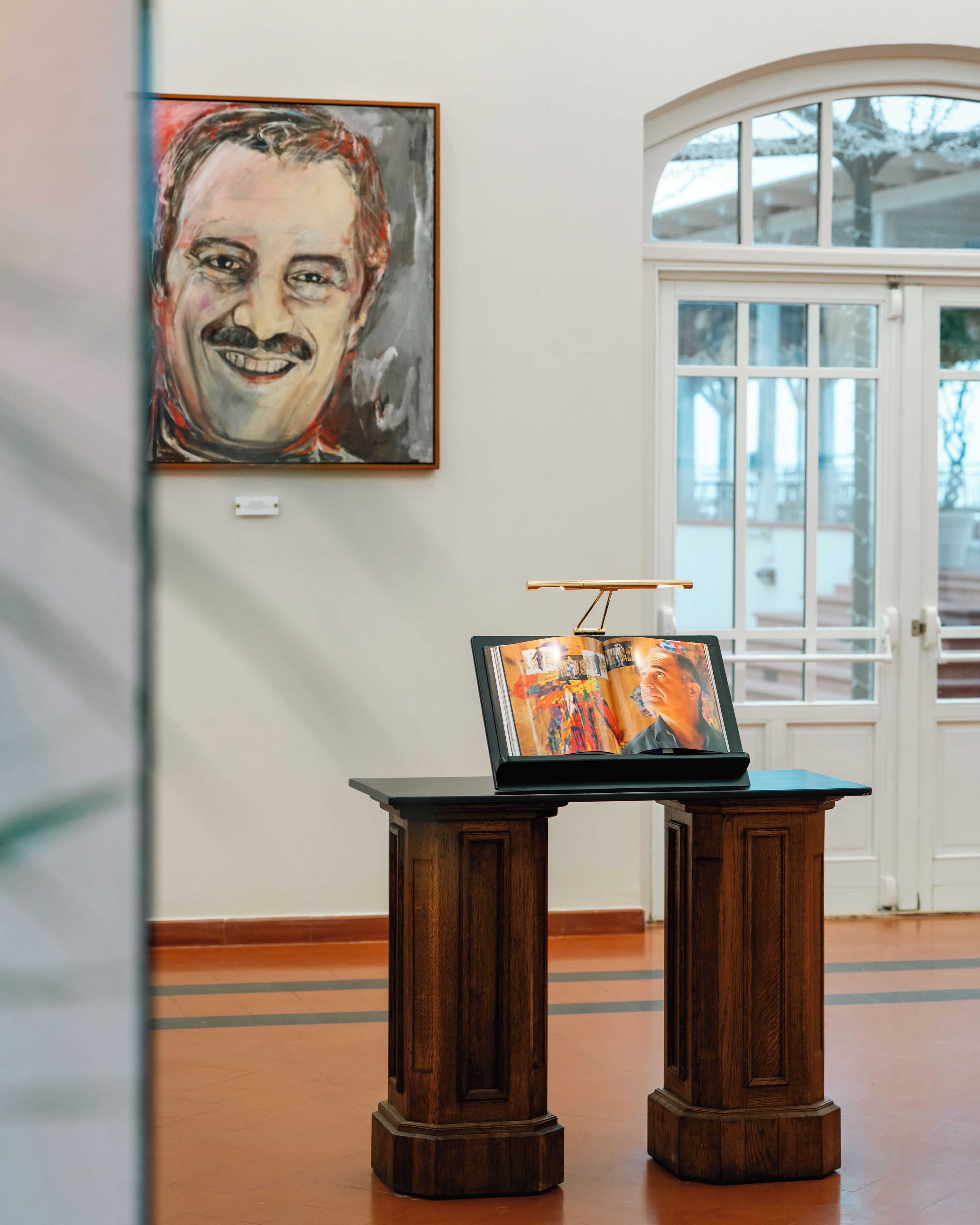 A wooden table with a laptop and a framed picture, set against a wall with a large painting.